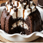 Indulgent Oreo Cookie Poke Cake – Easy, Fresh & Delicious 5 A tall slice of Cookies and Cream Cake layered with white chocolate mousse and topped with crushed Oreo cookies on a rustic plate in soft natural light.