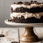 Cookies and Cream Cake – Easy, Fresh & Delicious 2 Homemade cookies and cream cake with layers of moist chocolate cake, cookies and cream buttercream frosting, and crushed Oreos on top, styled on a white cake stand with minimal kitchen decor