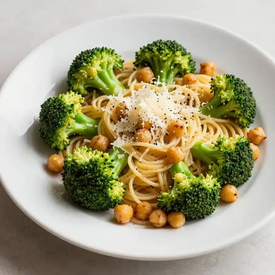 A bowl of broccoli chickpea pasta garnished with fresh herbs on a wooden table.