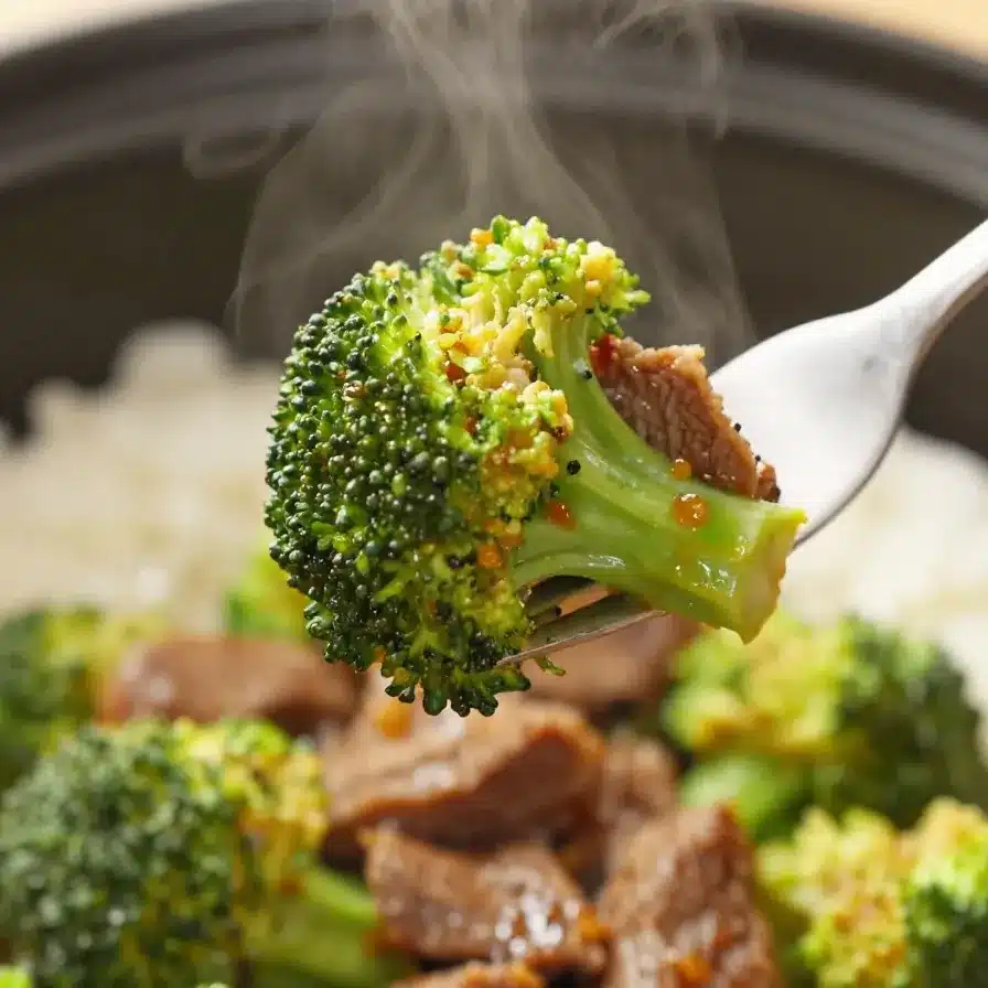 A plate of slow-cooked broccoli beef served with steamed white rice on a wooden table.